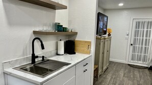 A modern kitchen with a sink, countertop, and cabinets. There is a wooden shelf above the sink and a television on the wall. - Cozy cottage in downtown Hamilton in the heart of the Bitterroot Valley.  (Hamilton)