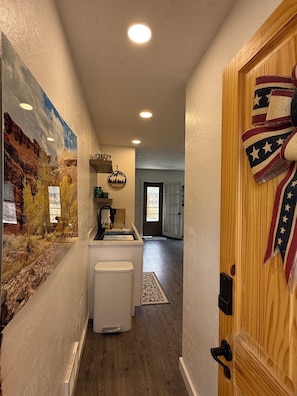 Un couloir avec un coin cuisine, une porte en bois ornée d’un drapeau et une fresque murale.