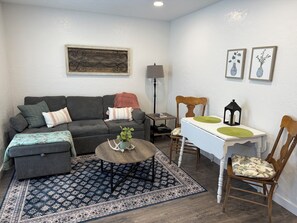 A living room with a sofa, ottoman, coffee table, chairs, a rug, a lamp, a table, and wall art.