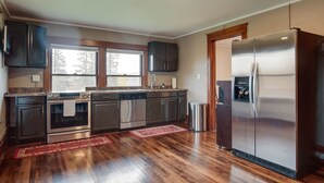 A modern kitchen with stainless steel appliances, dark wooden cabinets, and a red rug on the floor. - Spacious Home in Ramsay: 9 Smart TVs + Pool Table! (Ramsay)