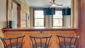 A kitchen with wooden cabinets, a bar counter, and three black bar stools. - Spacious Home in Ramsay: 9 Smart TVs + Pool Table! (Ramsay)