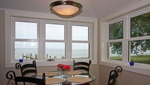 A dining area with a round glass table, four chairs, and a view of the sea through large windows. -  Artists, writers & creative minds  IMAGINE YOUR GETAWAY AT SIMPLICITY COTTAGE (Tilghman Island)