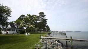A lakeside property with a house, a grassy lawn, a dock, and a stone wall. -  Artists, writers & creative minds  IMAGINE YOUR GETAWAY AT SIMPLICITY COTTAGE (Tilghman Island)