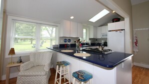 A compact kitchen with a central island, a dining area with a patterned sofa, and a small table with a lamp. -  Artists, writers & creative minds  IMAGINE YOUR GETAWAY AT SIMPLICITY COTTAGE (Tilghman Island)