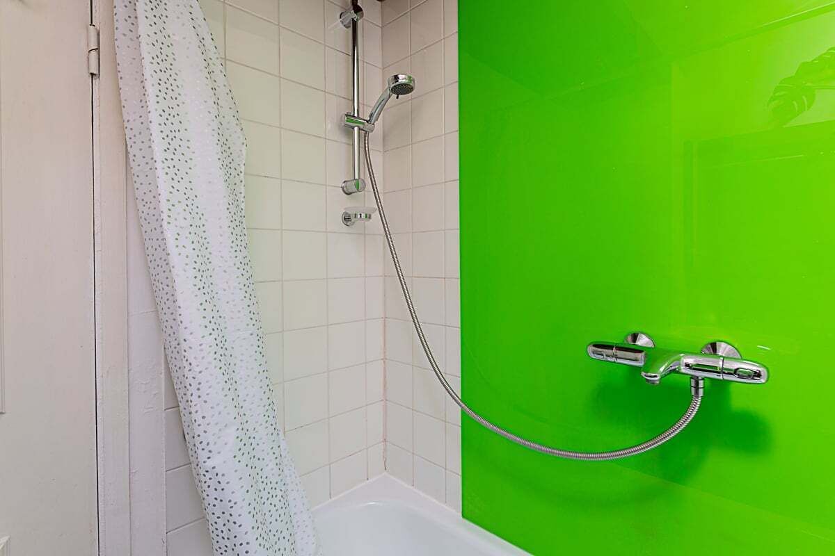 A bathroom with a shower, a white bathtub, and a green wall.