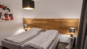 Une chambre moderne avec une tête de lit en bois, deux lits avec une literie à rayures, un luminaire suspendu et des lampes de chevet.
