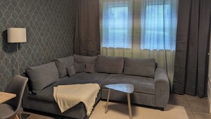 Un salon moderne avec un canapé d’angle gris, une petite table d’appoint et une lampe.