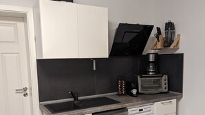 Une cuisine compacte avec des meubles blancs, un lave-vaisselle encastré, un réfrigérateur de petite taille, un four à micro-ondes et une machine à café.