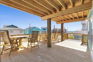 Um deck de madeira com mesa e cadeiras, com vista para uma área residencial com casas e o oceano.