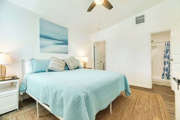 A bedroom with a bed, nightstands, a ceiling fan, a painting, and a bathroom door. - Family Beach Retreat Steps From Surfside Waves (Surfside Beach)