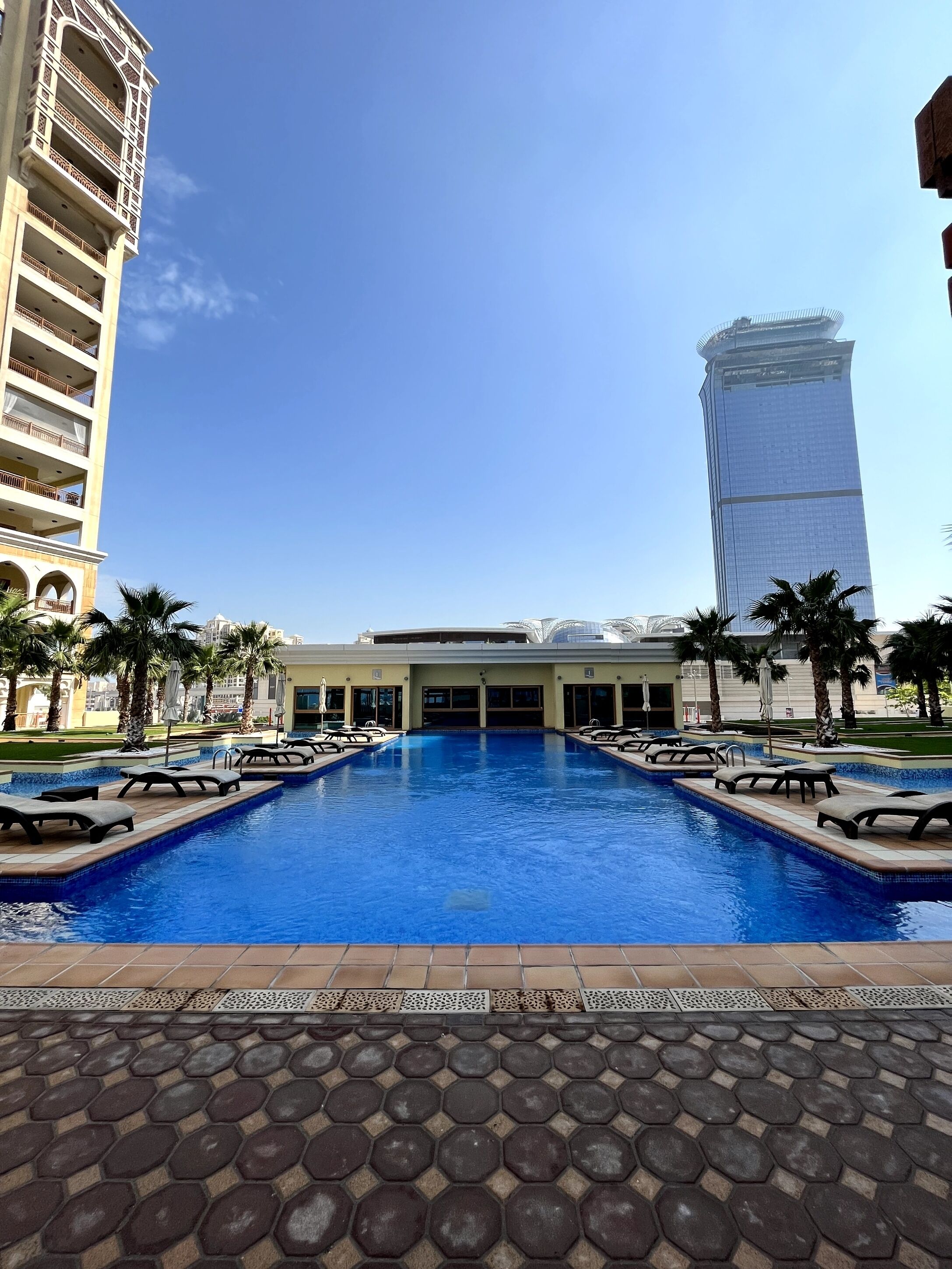 Una piscina con borde de azulejos, un edificio de diseño moderno y palmeras.