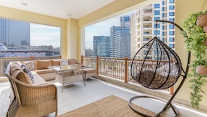 A balcony with wicker furniture, a hanging chair, and a view of city buildings.