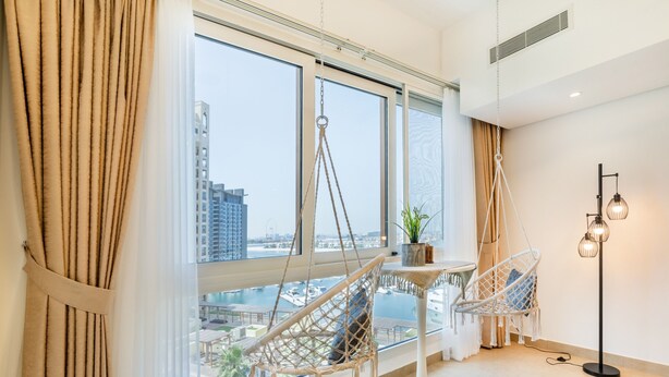 A modern room with large windows, a hanging chair, a floor lamp, and a small table with a plant.