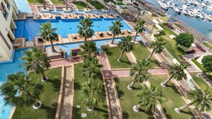 A resort with a large swimming pool, palm trees, and a marina with boats.