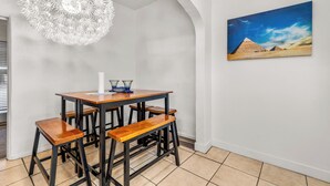 Un coin repas avec une table et des bancs en bois, un lustre blanc et un tableau représentant des pyramides au mur.