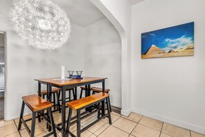 A dining area with a wooden table and benches, a white chandelier, and a painting of pyramids on the wall.
