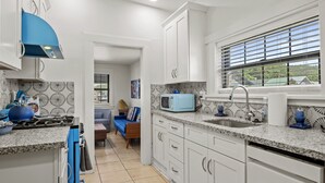 Une cuisine moderne avec des meubles blancs, un poêle bleu et un four à micro-ondes. Une fenêtre avec des stores offre une vue sur la verdure à l’extérieur.