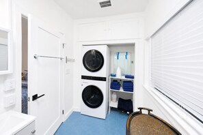 A compact laundry room with two stacked washing machines, a drying rack, and neatly folded towels on shelves.