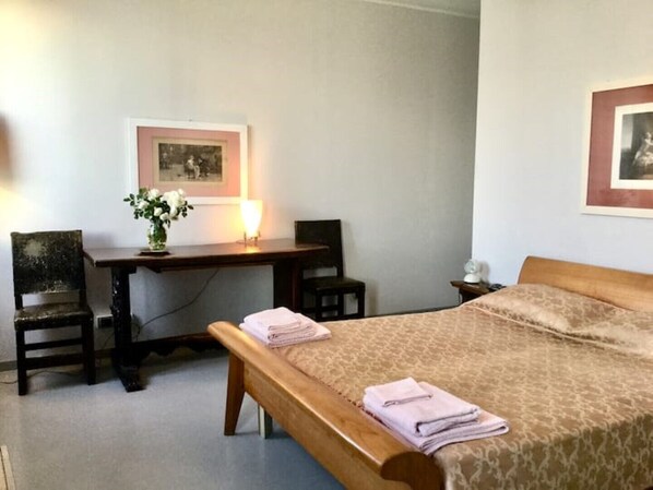 Ein Hotelzimmer mit einem Holzbett, einem Schreibtisch mit Lampe, zwei Stühlen und einem gerahmten Bild an der Wand.