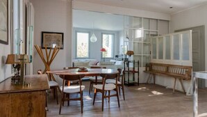 A dining area with a wooden table and chairs, a kitchen in the background, and large windows allowing natural light. - Canal Views and a Secret Garden in Giudecca (Venezia)