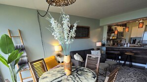 Een eetgedeelte met een ronde tafel, stoelen, een vaas met bloemen, een hanglamp en een keuken op de achtergrond.