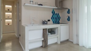 A modern kitchen with white cabinetry, a granite countertop, and a built-in oven. There are shelves above the sink holding glassware and jars. - Cozy House close to the sea (Foxi Lioni)