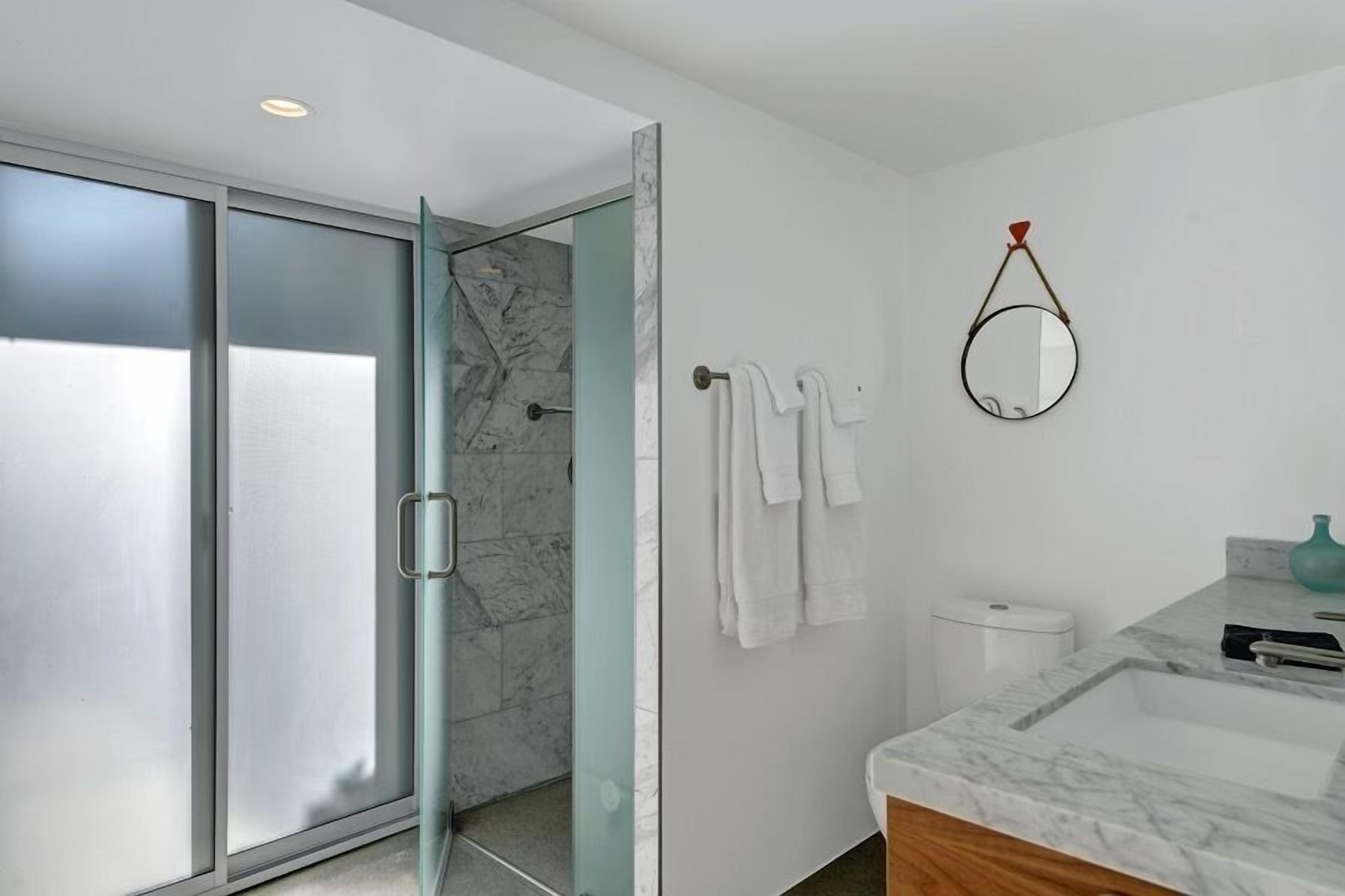 A modern bathroom with a glass shower door, a marble sink, and a round mirror.
