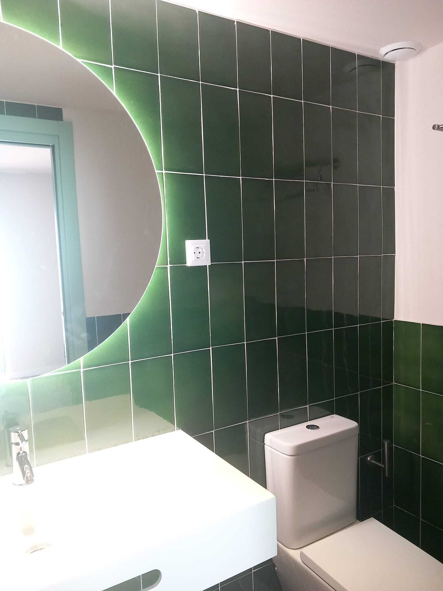 Kylpyhuone, jonka seinät on päällystetty vihreillä laatoilla, ja jossa on valkoinen pesuallas ja wc-istuin.