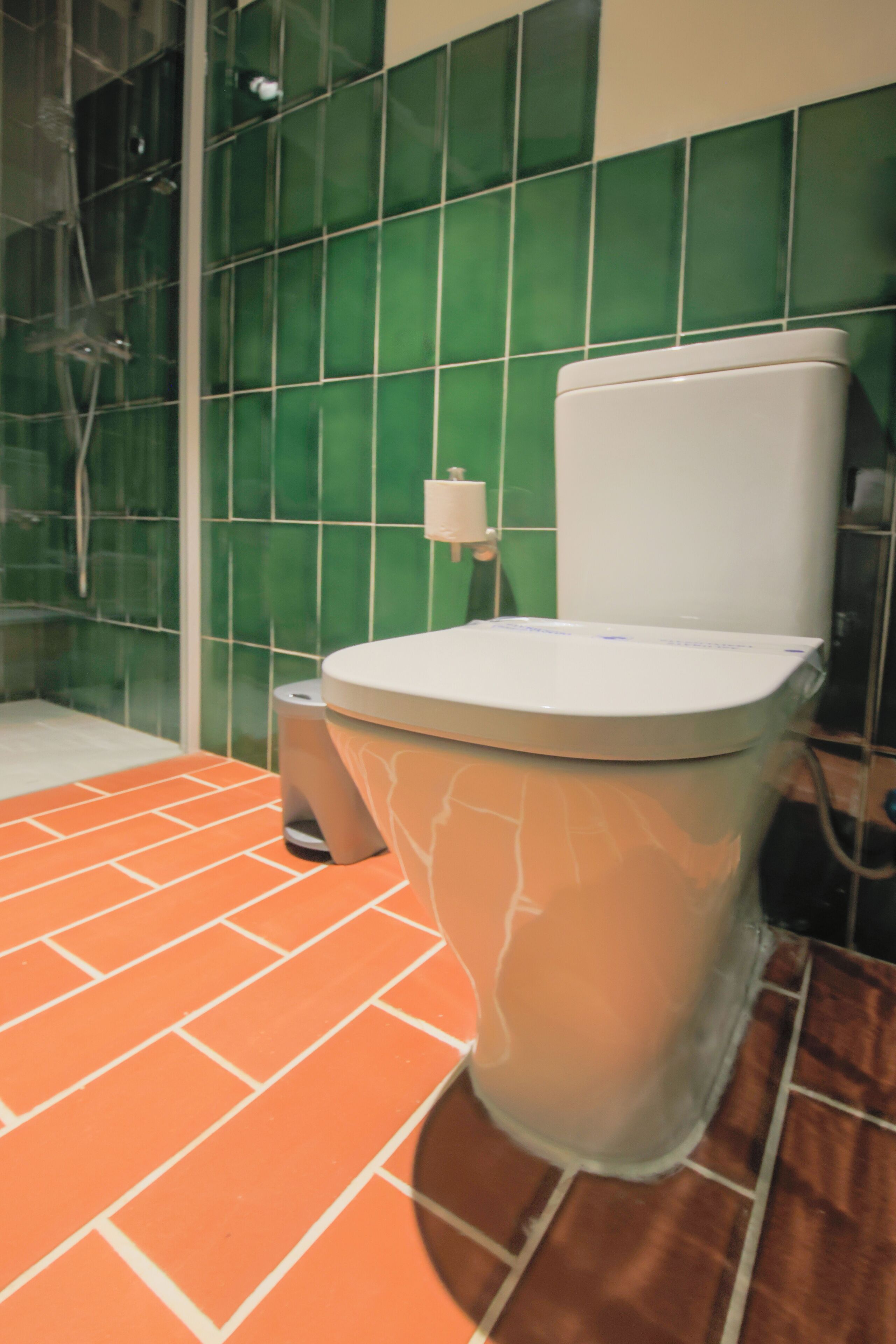 A bathroom with a toilet, a trash bin, and a shower area.