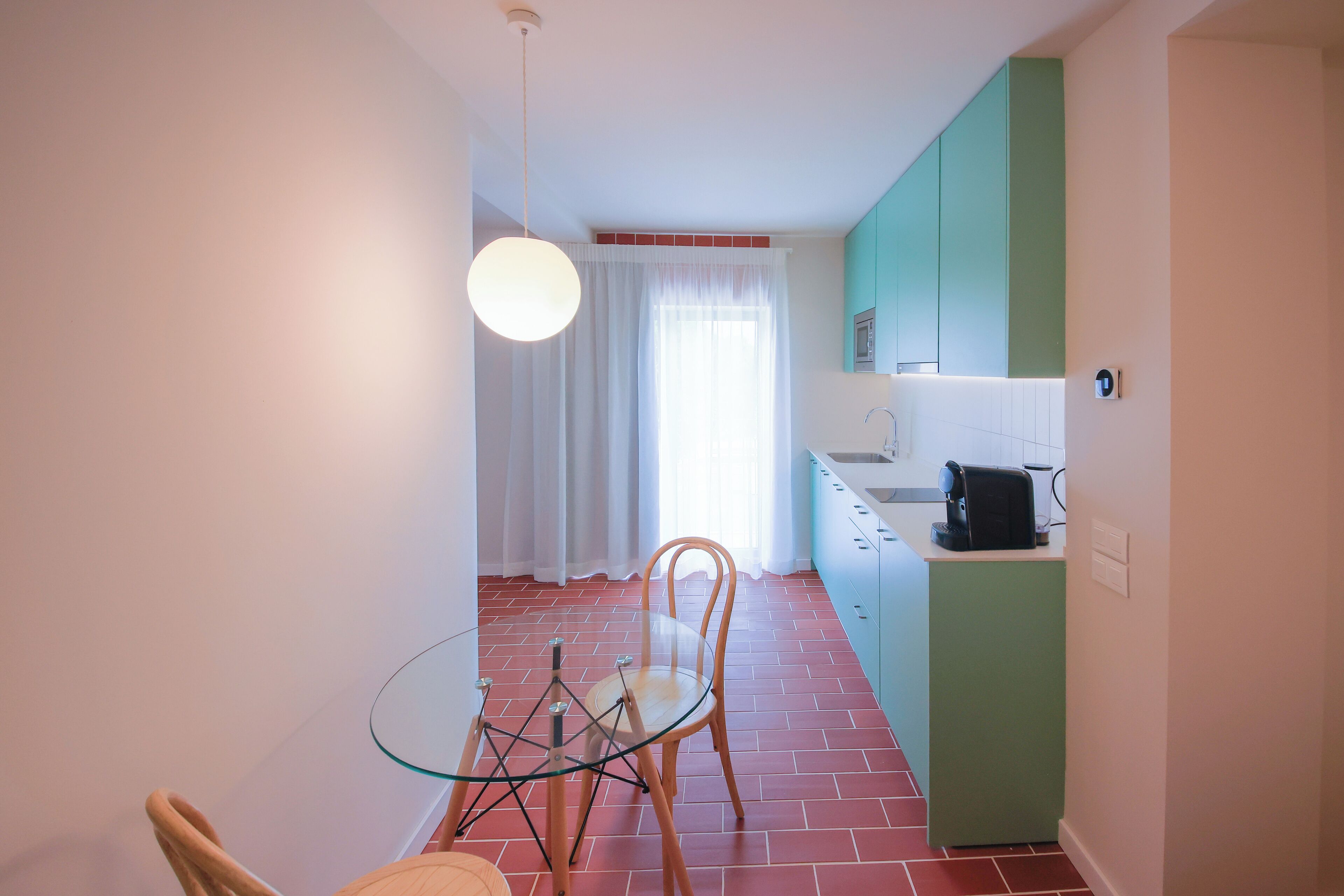 A compact kitchen with a dining table and chairs, a hanging light fixture, and a window with curtains.