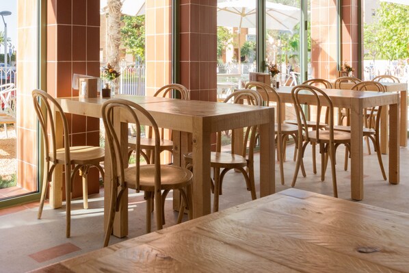 A restaurant with wooden tables and chairs, large windows, and a view of the outside. - Aparthotel Terra Aurea (Salou)