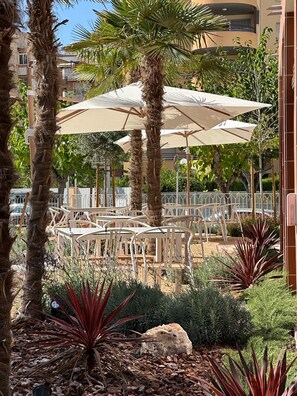 An outdoor seating area with tables and umbrellas, surrounded by palm trees and various plants. - Aparthotel Terra Aurea (Salou)