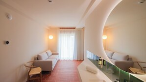A modern hotel room with a large mirror, a sofa, a chair, and a bathroom with a sink and mirror. - Aparthotel Terra Aurea (Salou)