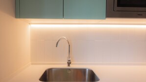 A kitchen with a stainless steel sink, teal cabinets, and white subway tiles. - Aparthotel Terra Aurea (Salou)