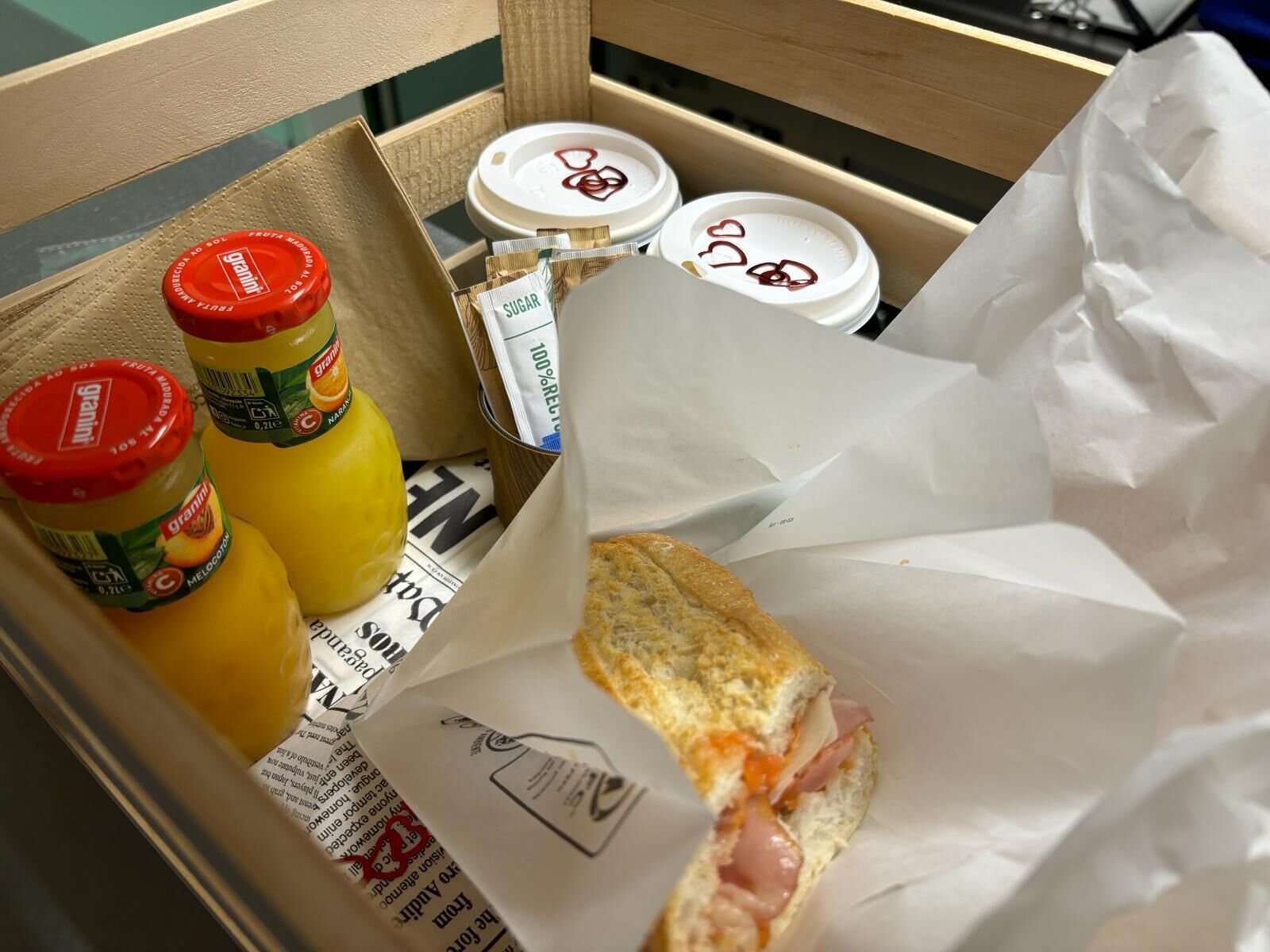 Una caja con un sándwich, dos botellas de Granini y sobrecitas de azúcar.