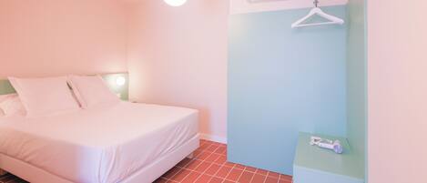 A neatly made bed in a room with a tiled floor, an air conditioning unit, and a hanging clothes rack.