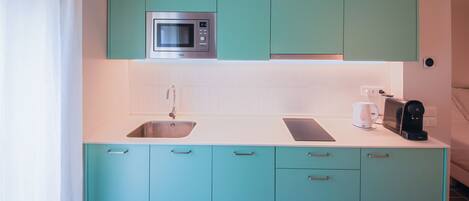 Una cocina con gabinetes verde azulado, un microondas de acero inoxidable, un fregadero y una cafetera.