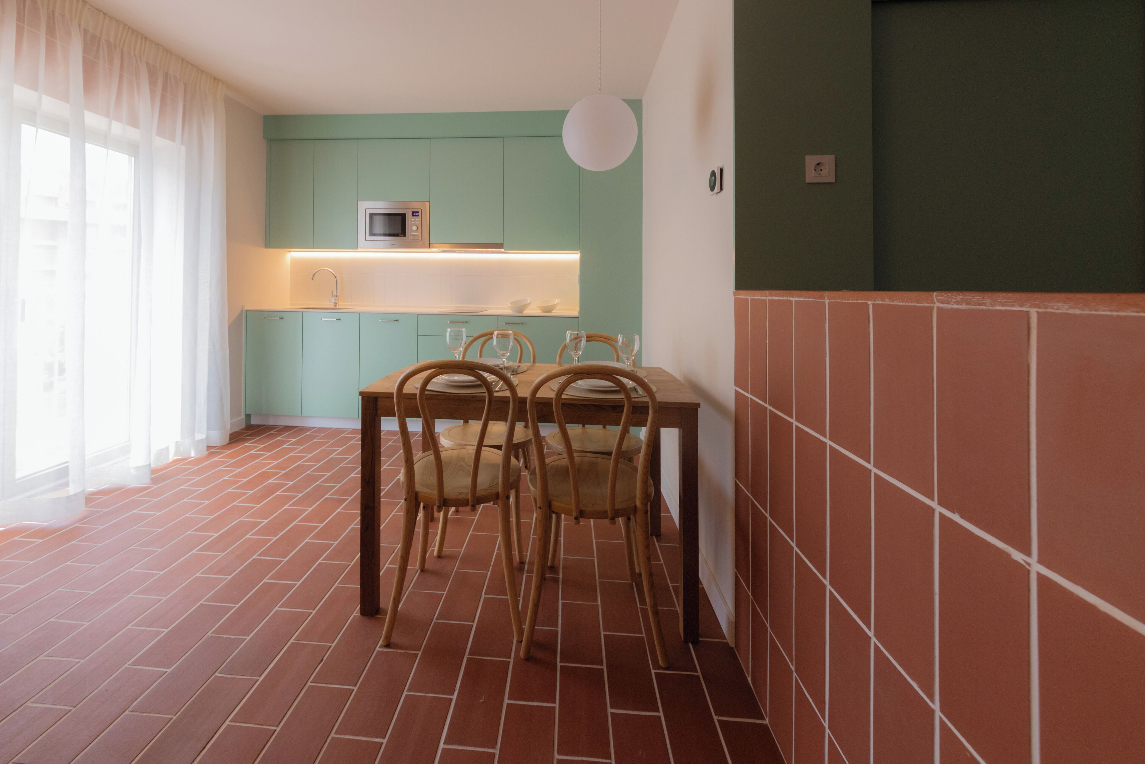 A dining area with a table and chairs, a kitchen with teal cabinets, and a tiled floor.