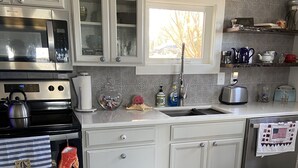 A modern kitchen with white cabinetry, stainless steel appliances, and a window above the sink. - Bubba Butler's Cottage (Locust Hill)