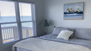A bedroom with a large bed, a painting of sailboats on the wall, and a window with blinds. - Bubba Butler's Cottage (Locust Hill)