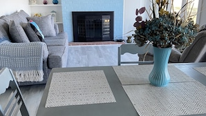 A living room with a fireplace, a dining table with placemats, and a blue vase with flowers. - Bubba Butler's Cottage (Locust Hill)