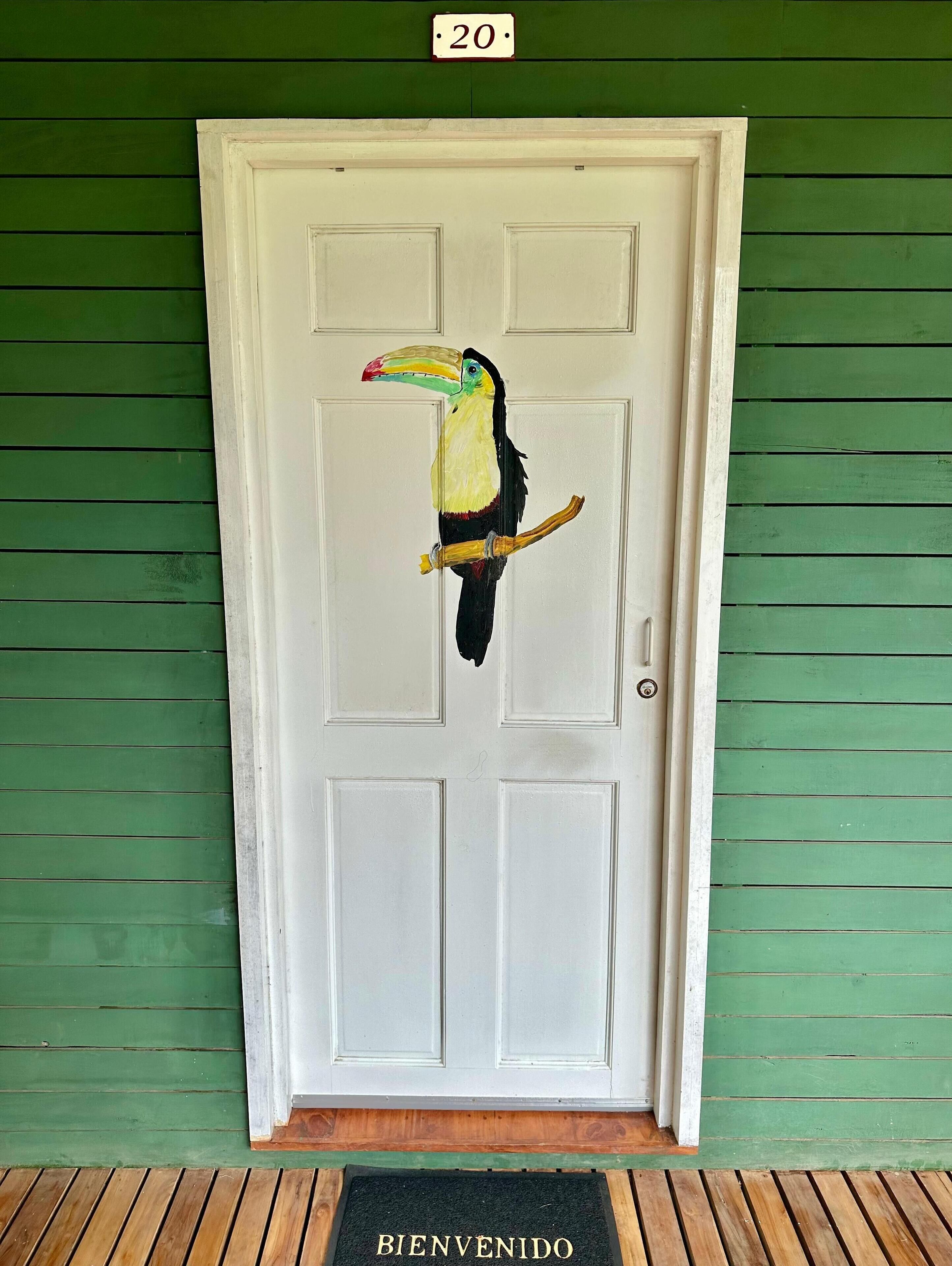 A door with a toucan painting, a green wall, and a welcome mat.