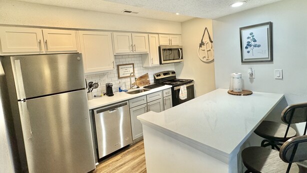 A modern kitchen with white cabinets, stainless steel appliances, and a central island with bar stools. - Mid city huntsvegas studio #2 (Huntsville)