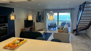 Un salon moderne comprenant un coin repas, une cuisine et un balcon avec vue sur la mer.