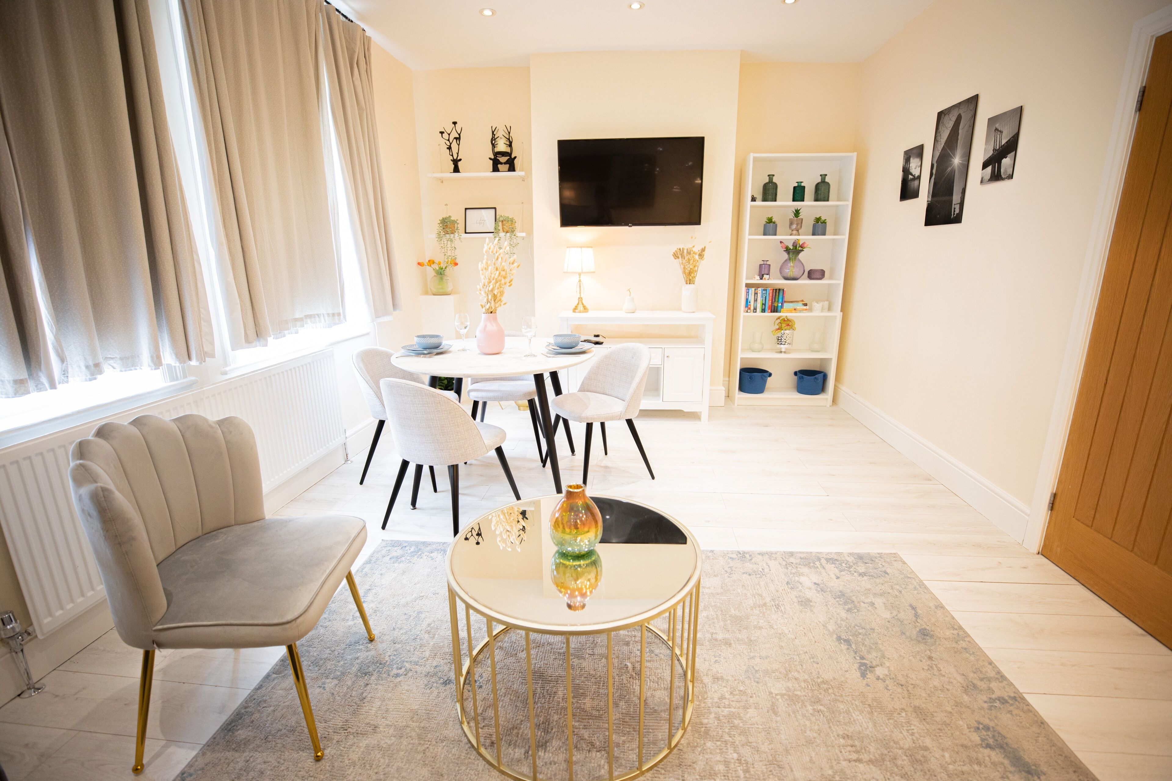 Una sala moderna con una mesa de centro redonda, dos sillones, una mesa de comedor con sillas, un televisor montado en la pared y una estantería.