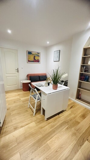 Una habitación moderna y luminosa con un escritorio blanco, una silla, un sofá, una estantería y una planta en maceta.