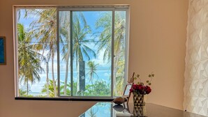 A room with a large window offering a view of palm trees and the ocean. - Pousada dos Corais (Trairi)