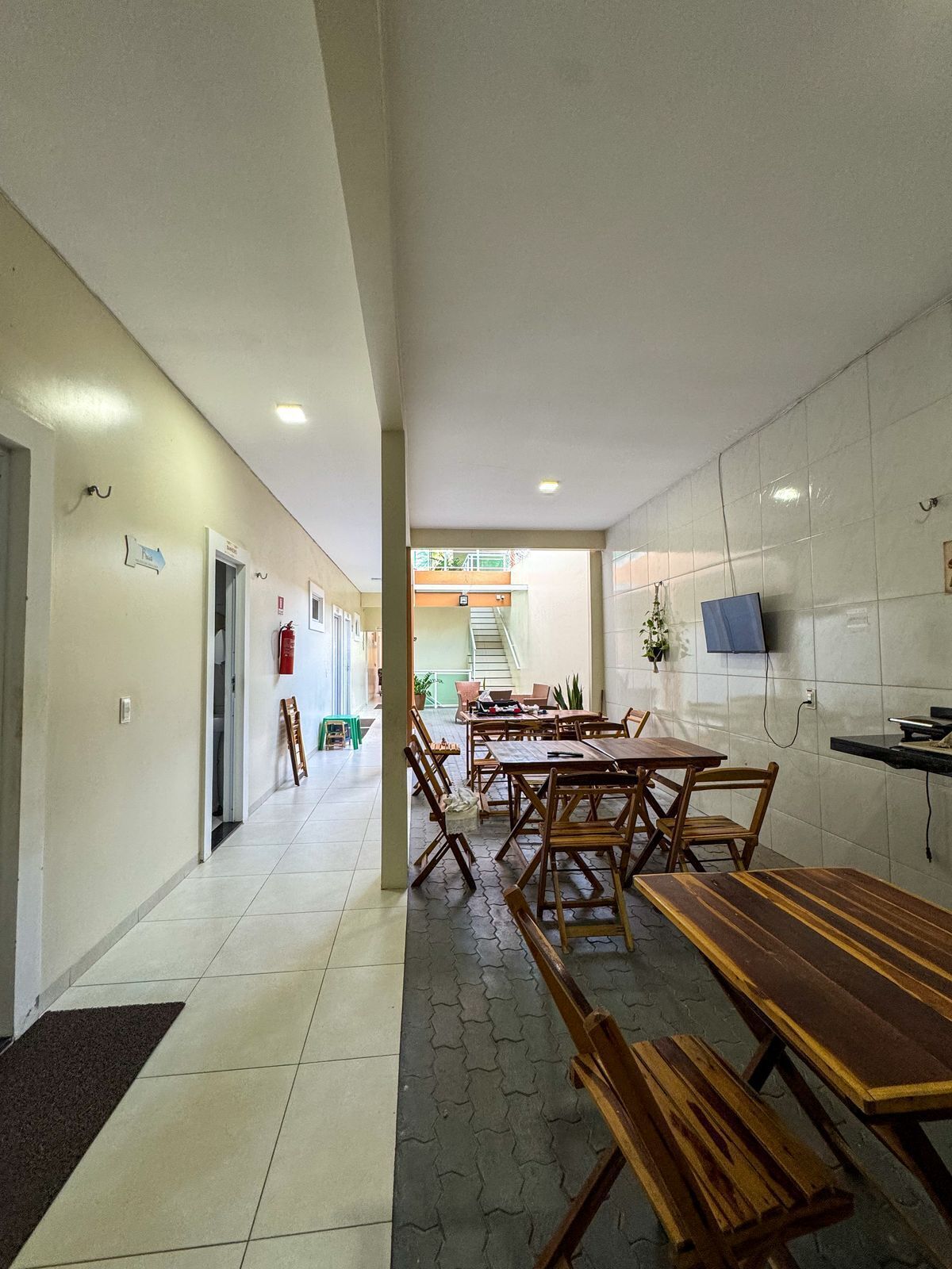 A hallway with a dining area featuring wooden tables and benches, a staircase leading to an upper level, and a fire extinguisher on the wall.