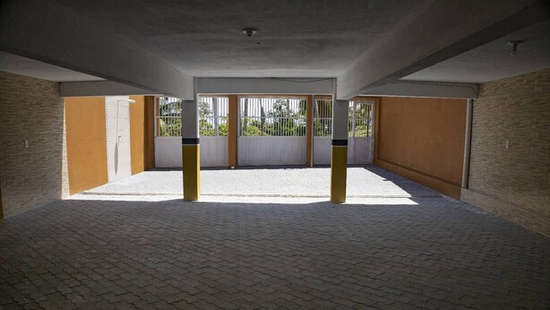 An empty corridor with tiled flooring, a concrete ceiling, and a view of a building with barred windows. - Pousada dos Corais (Trairi)