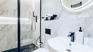 Un baño moderno con ducha envuelta en vidrio, un espejo redondo y un lavabo blanco con grifo negro.